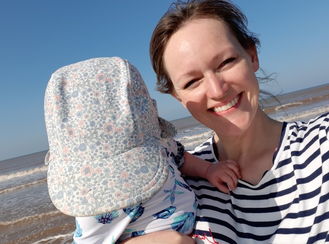 Lindsey Alvis, in a stripey top, holds her daughter on a bright day at the seaside.