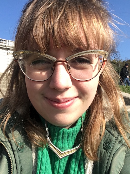 Close-up selfie of a white woman with fair hair, glasses and a green jumper