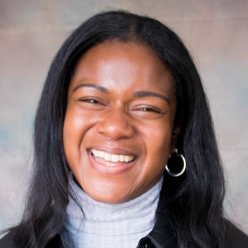 Headshot of a smiling Black woman, with long black hair, hoop earrings and white turtleneck