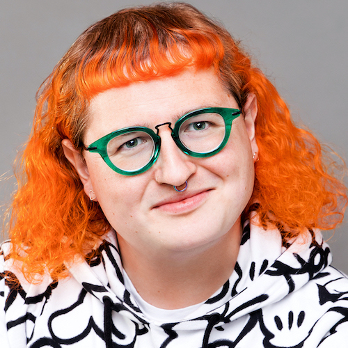 Headshot of Tabby Lamb with long vivid orange hair and green rimmed glasses