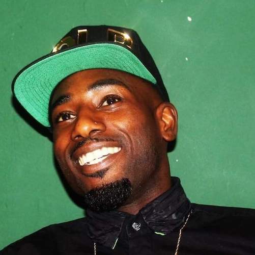 A black man in a green and black cap against a green wall