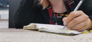a woman writes in an A5 notebook with a silver mechanical pencil on a wooden desk