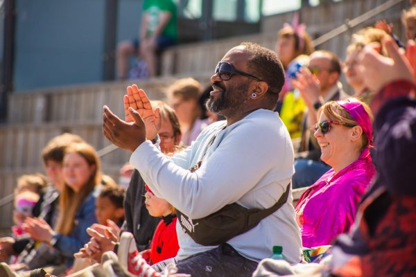 A black man in a white, long-sleeved top, and black sunglasses gives a standing ovation.