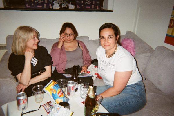 Three women sat on the couch, two are engaging in conversation and the other is smiling at the camera.
