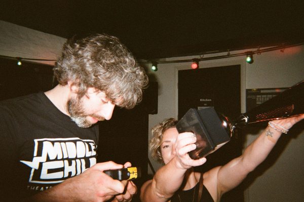 A man looks down at a disposable camera whilst a woman holds a trophy in the air obscuring half her face.