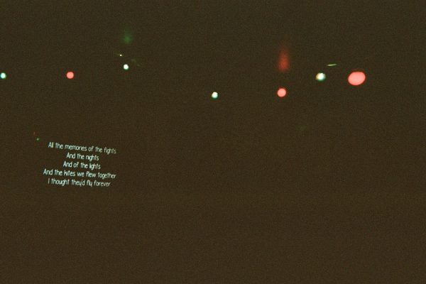 A largely black image with white writing poking out of the darkness on the left side along with green and red light bulbs across the top of the picture.