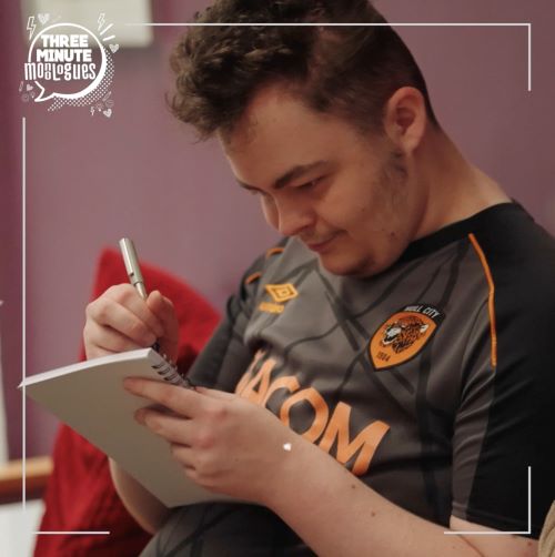 A young white man in a Hull City shirt writes in a notebook