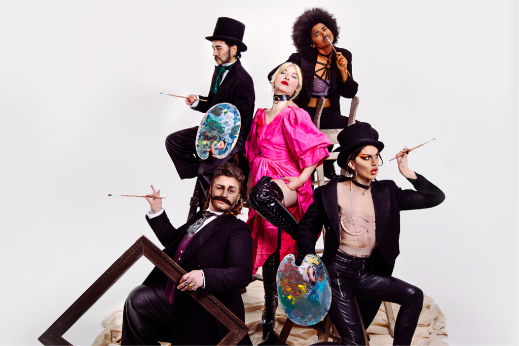 A woman in vivid pink Victorian dress stands confident and cocksure with her hand on her hip, surrounded by four drag kings in tail coats. Two of the drag kings wear top hats, another has Afro hair style and another a long flowing mullet. The four drag kings variously hold paintbrushes, an empty picture frame and messy paint palettes.
