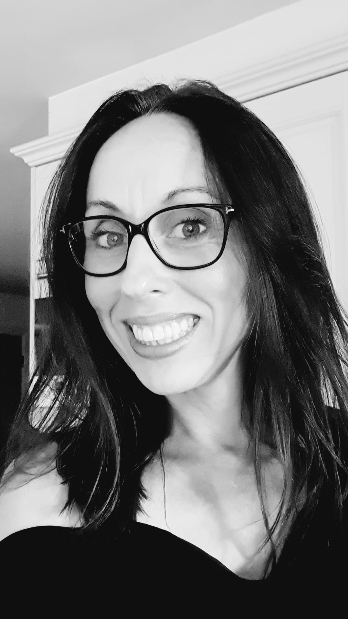 A black and white selfie of a white woman with dark shoulder length hair and large black glasses.